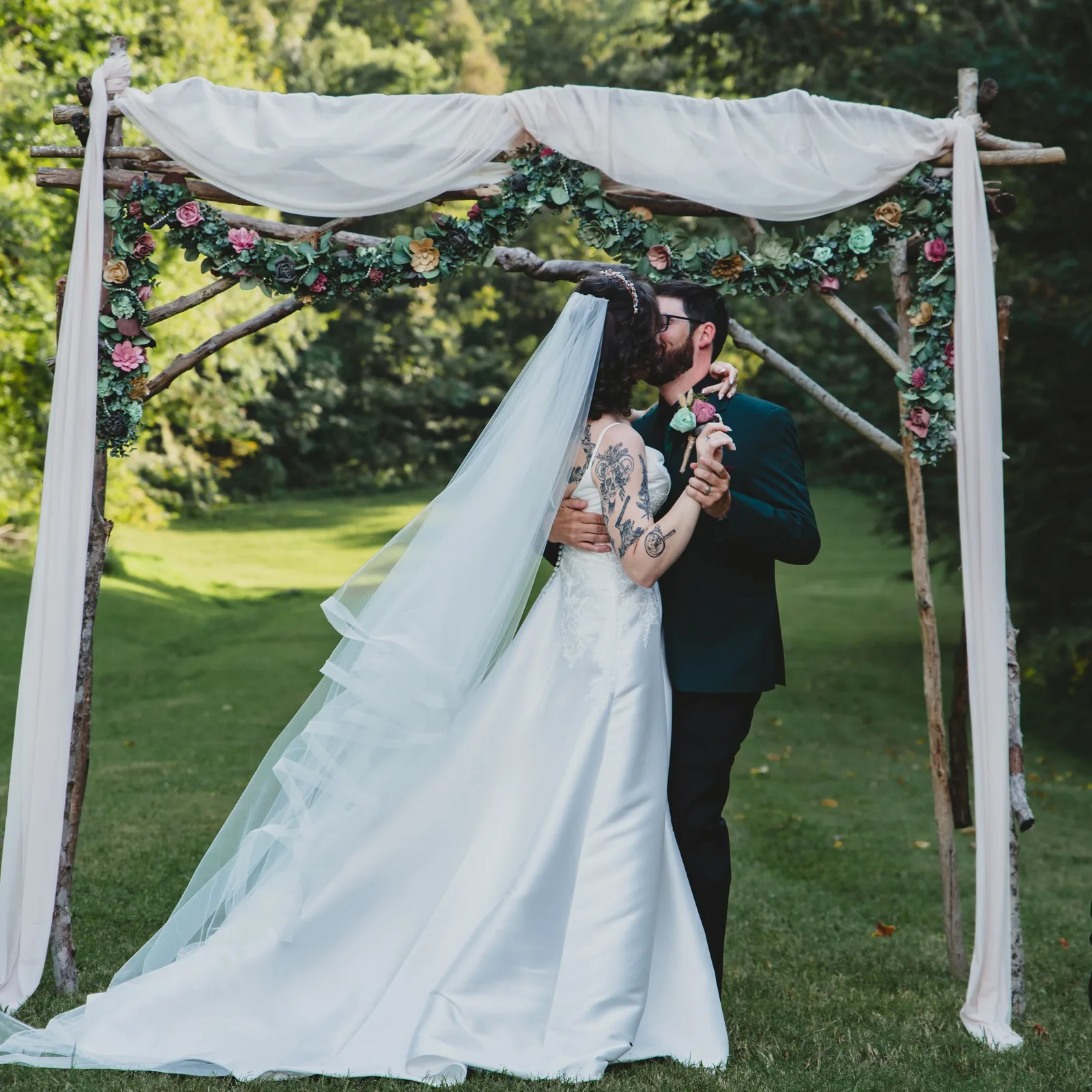 Weekday elopement in Sevierville, TN: a couple sharing a kiss alone under the draped arch in the Wooded Cove at The Barn at Chestnut Springs in Sevierville, TN