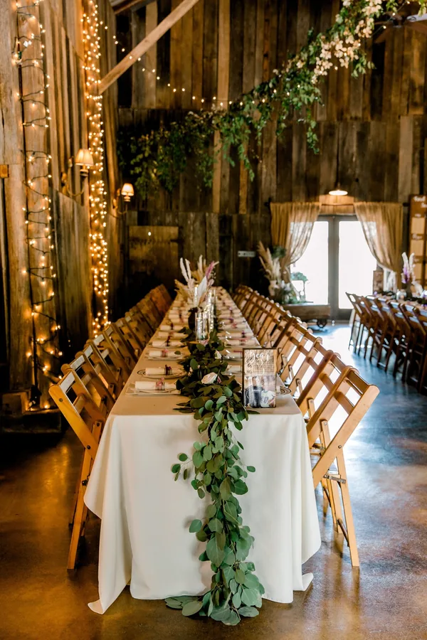 Long tables with eucalyptus garland and candles set for a reception inside the barn near Knoxville, TN